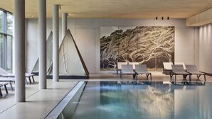 A modern indoor swimming pool with clear water, surrounded by lounge chairs and a large abstract mural on the wall. - natürlich Hell. Aparthotel & Camping (Fuegen)