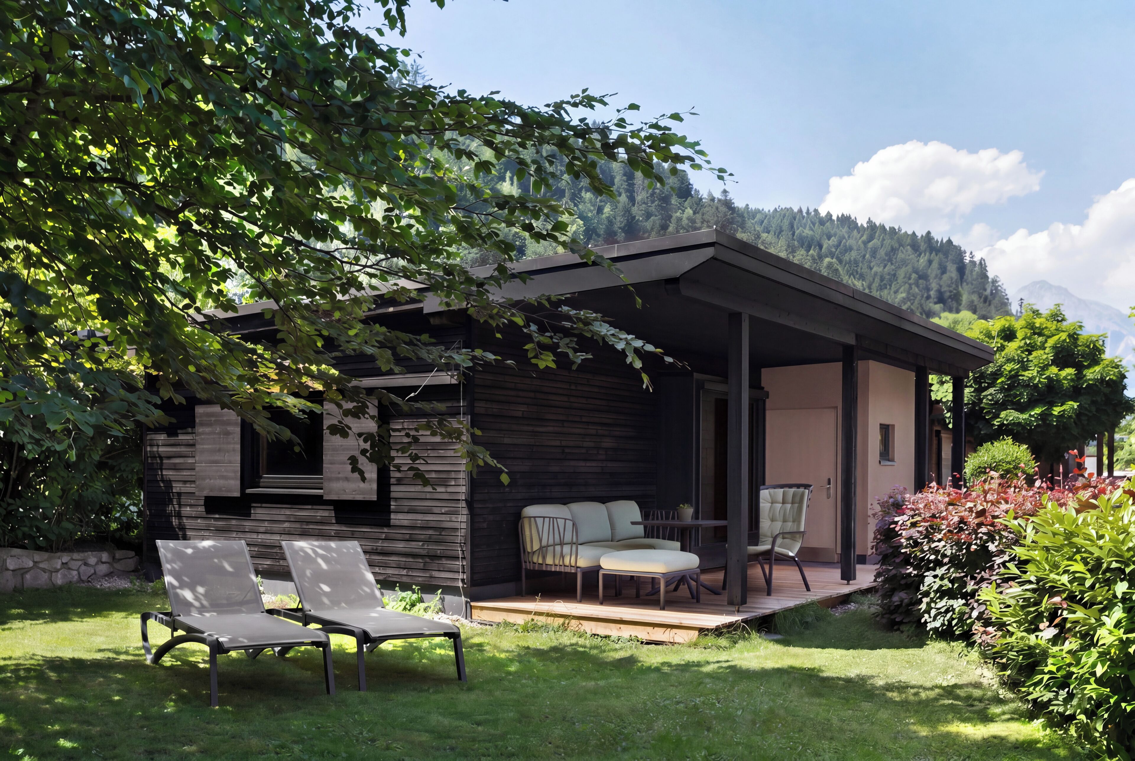 Un espacio exterior moderno con dos sillones de descanso y una mesa, rodeado de abundante vegetación y montañas al fondo.