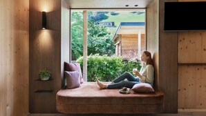A cozy seating area with a built-in bench, a TV mounted on the wall, and a view of a house and greenery outside. - natürlich Hell. Aparthotel & Camping (Fuegen)