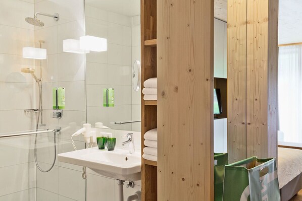 Un baño moderno con cabina de ducha de vidrio, lavabo con espejo y estantes de madera.