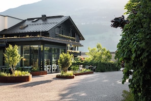 A building with a modern glass facade, a wooden exterior, and a cobblestone courtyard. - natürlich Hell. Aparthotel & Camping (Fuegen)