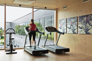 Un gimnasio con cintas de correr, una bicicleta estática y un ventanal con vistas a un edificio y árboles.