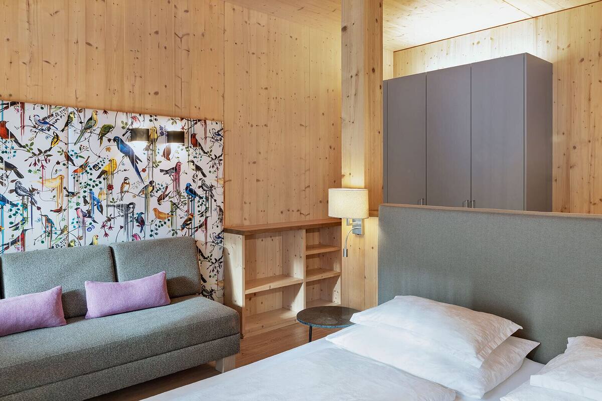 A hotel room with a wooden wall, a sofa, a bed, and a wardrobe.