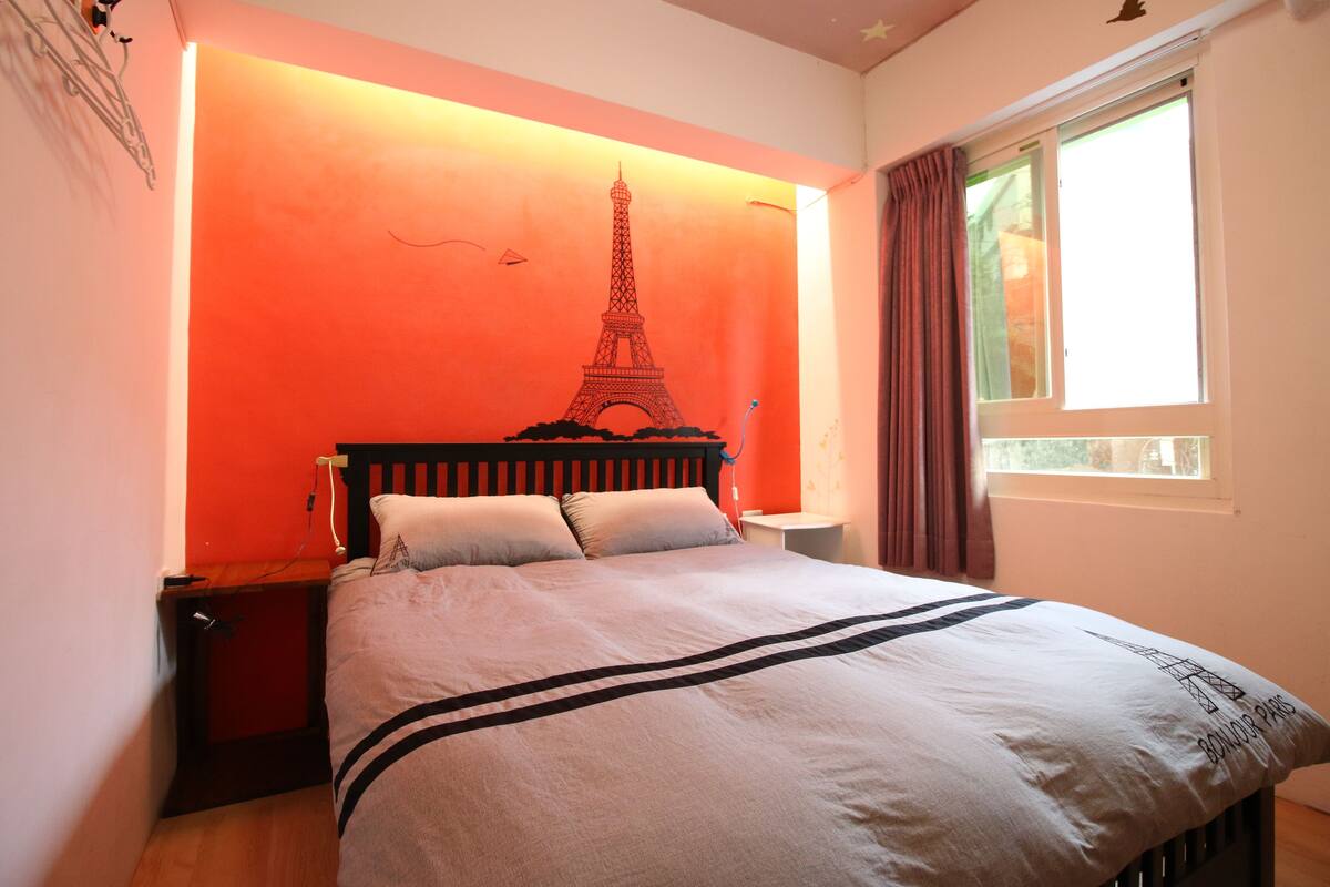 A bed with a headboard featuring the Eiffel Tower design, a bedside table, and a window with curtains.