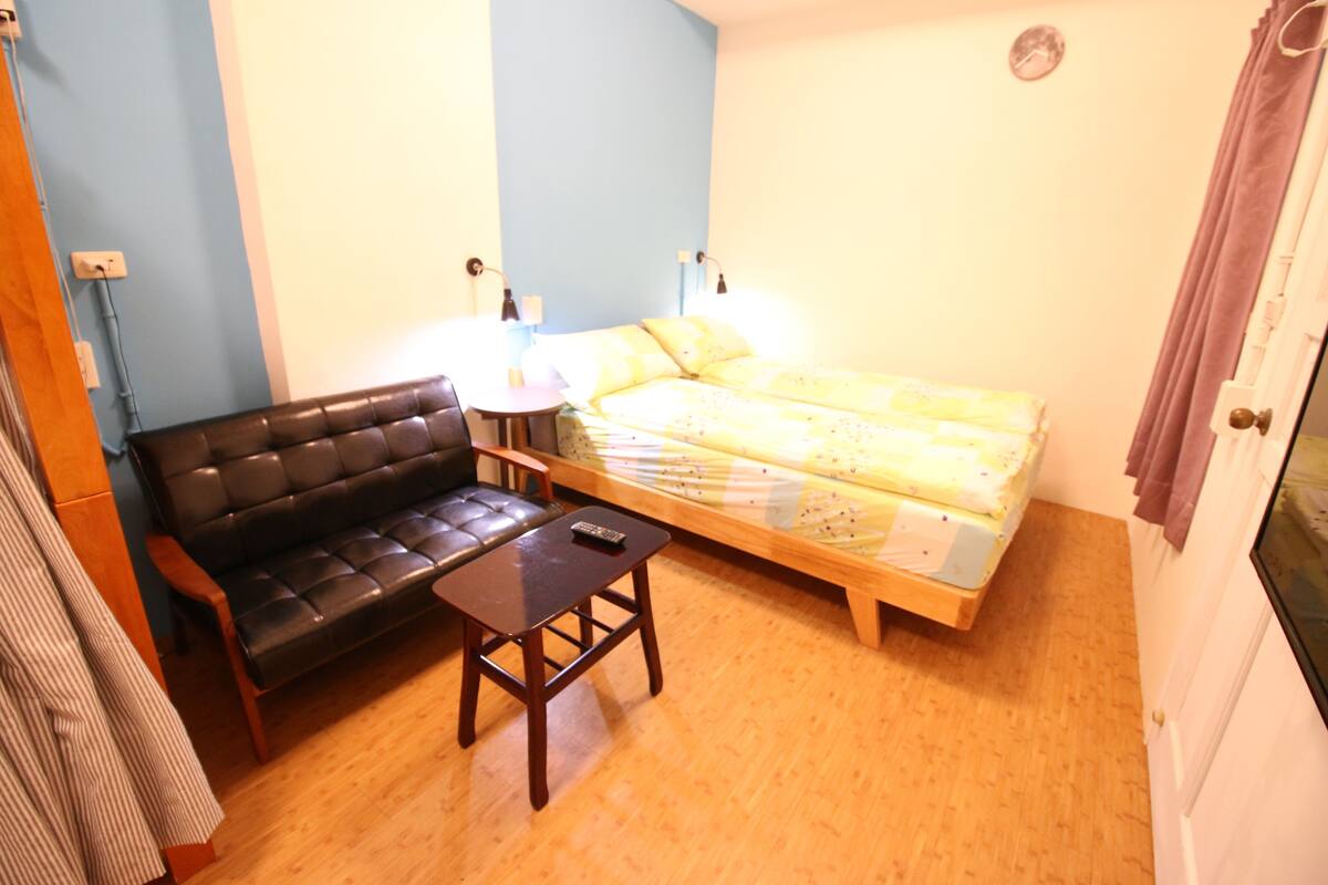 A small room with a bed, a sofa, a table, and a lamp.