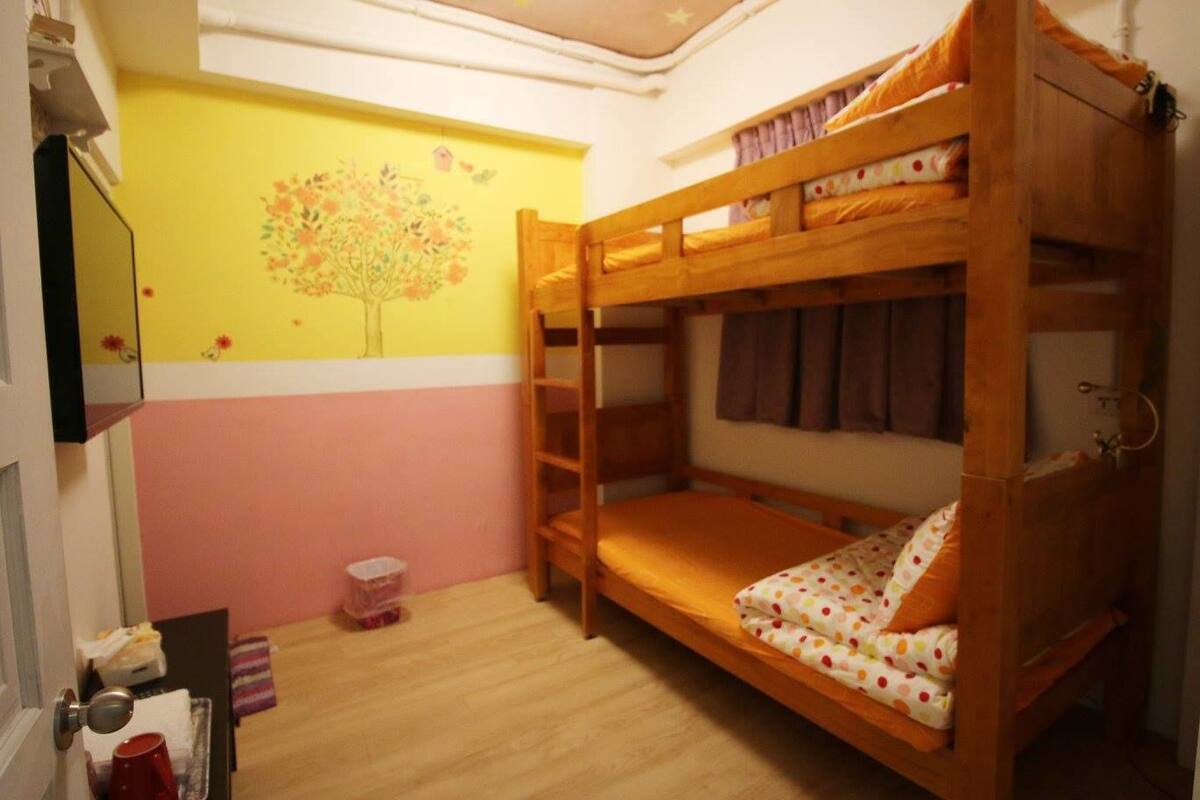 A bunk bed room with a wooden bunk bed, a small stool, and a wall decoration.