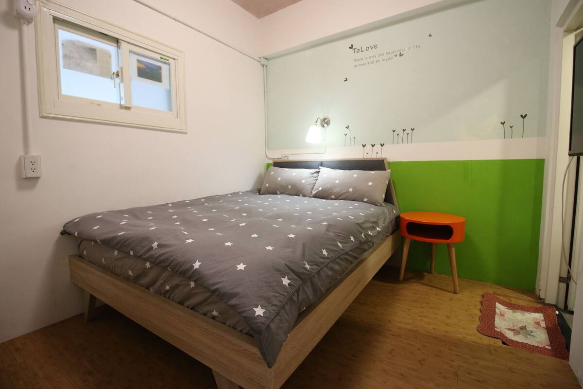A bedroom with a bed, a window, a green wall, and a motivational quote.