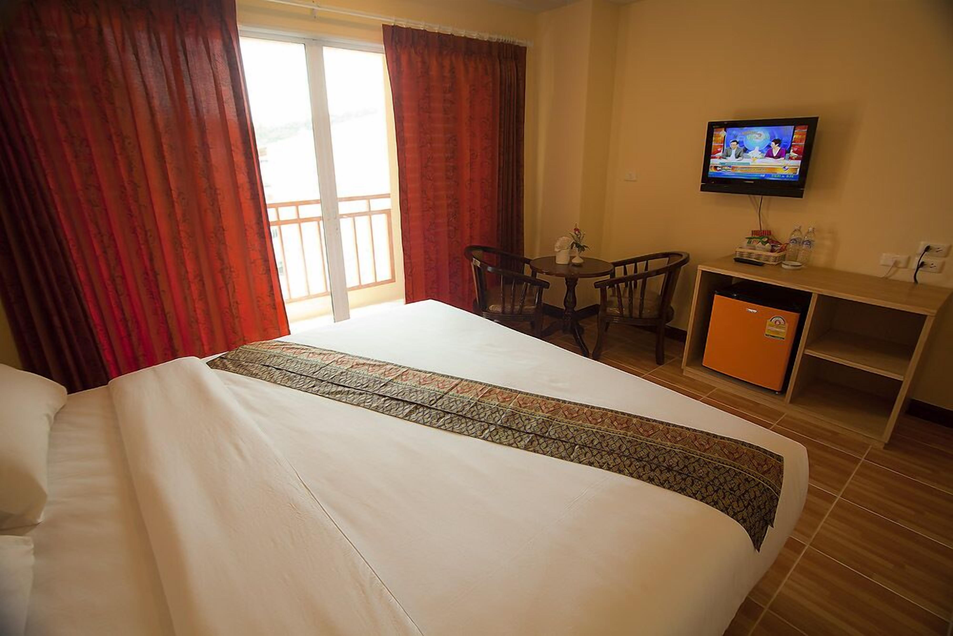 A hotel room with a large bed, a desk with a television, and a small refrigerator.