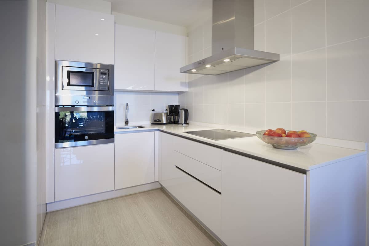 A modern kitchen with white cabinetry, a built-in microwave, a coffee maker, and a bowl of fruit on the counter.
