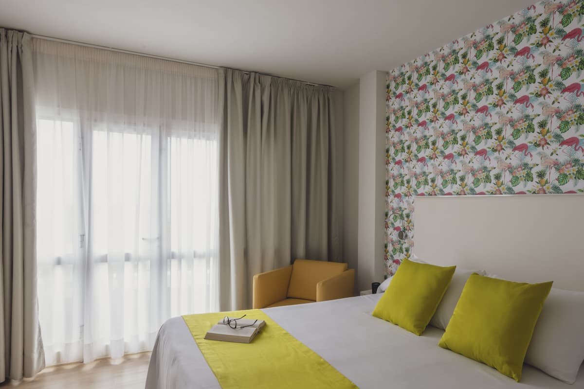 A hotel room with a large bed, a chair, and a window with sheer curtains.