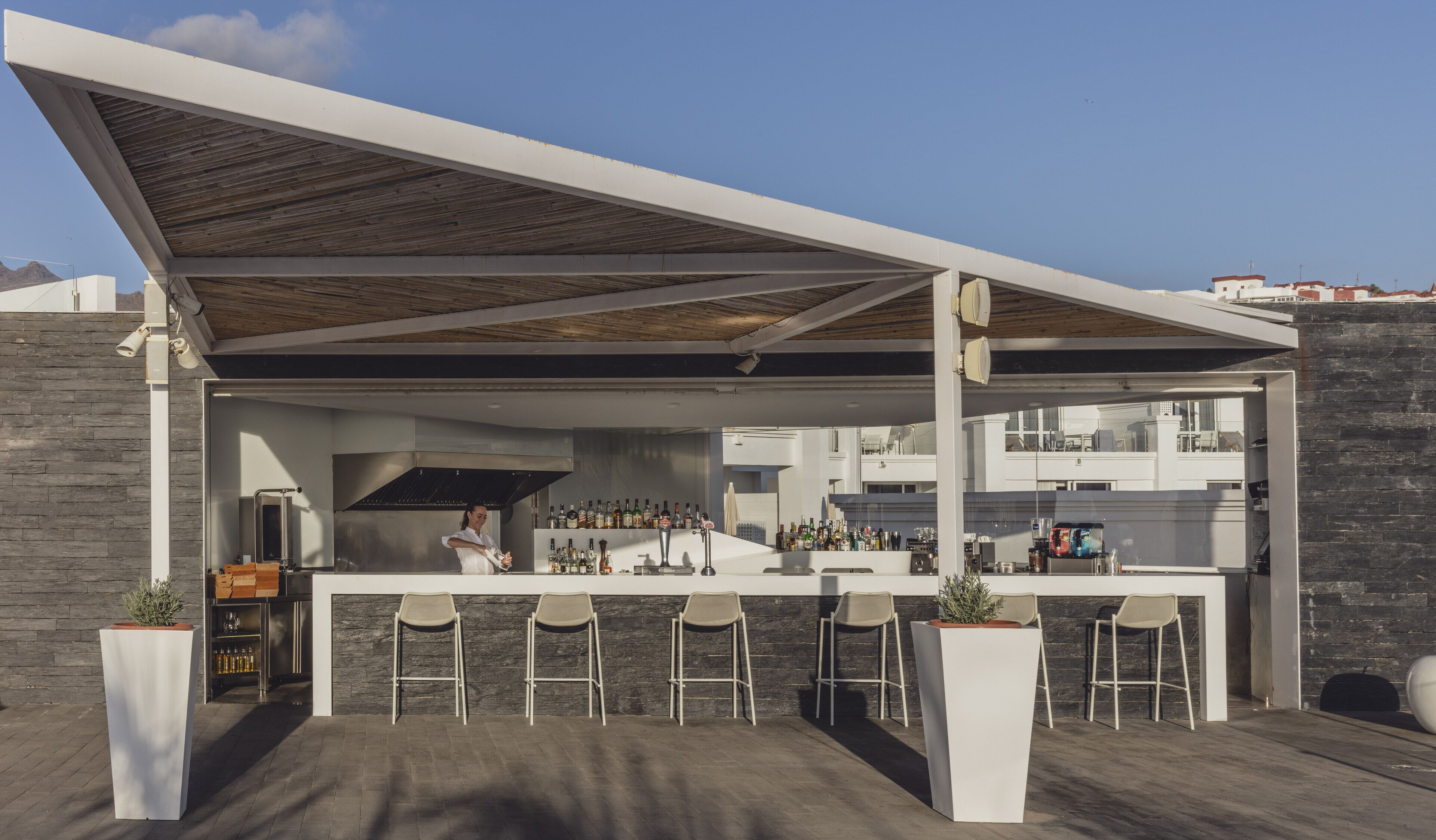 An outdoor bar area with a chef preparing drinks, a bar counter, and several stools.