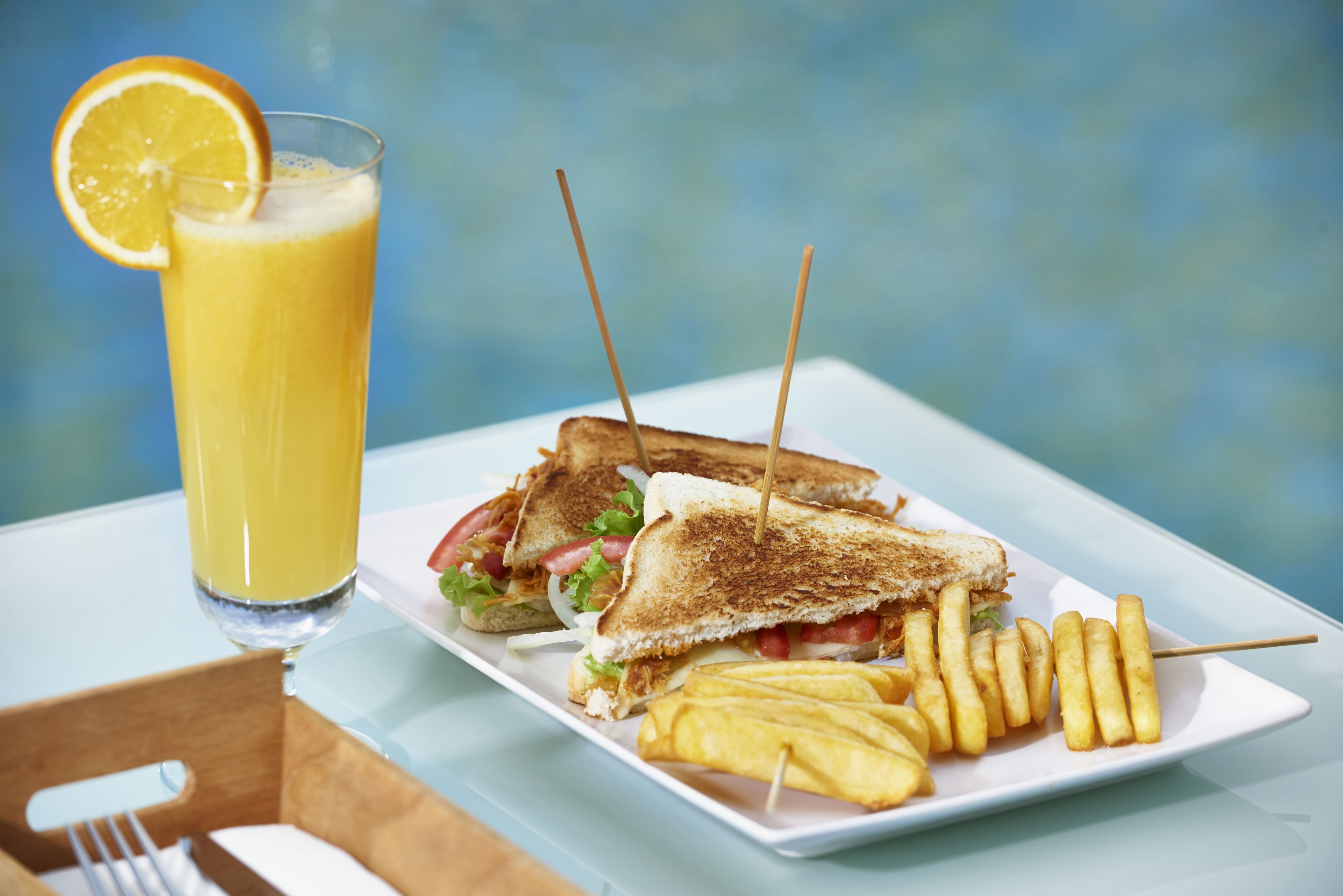 A sandwich with a side of fries and a glass of orange juice on a white plate.