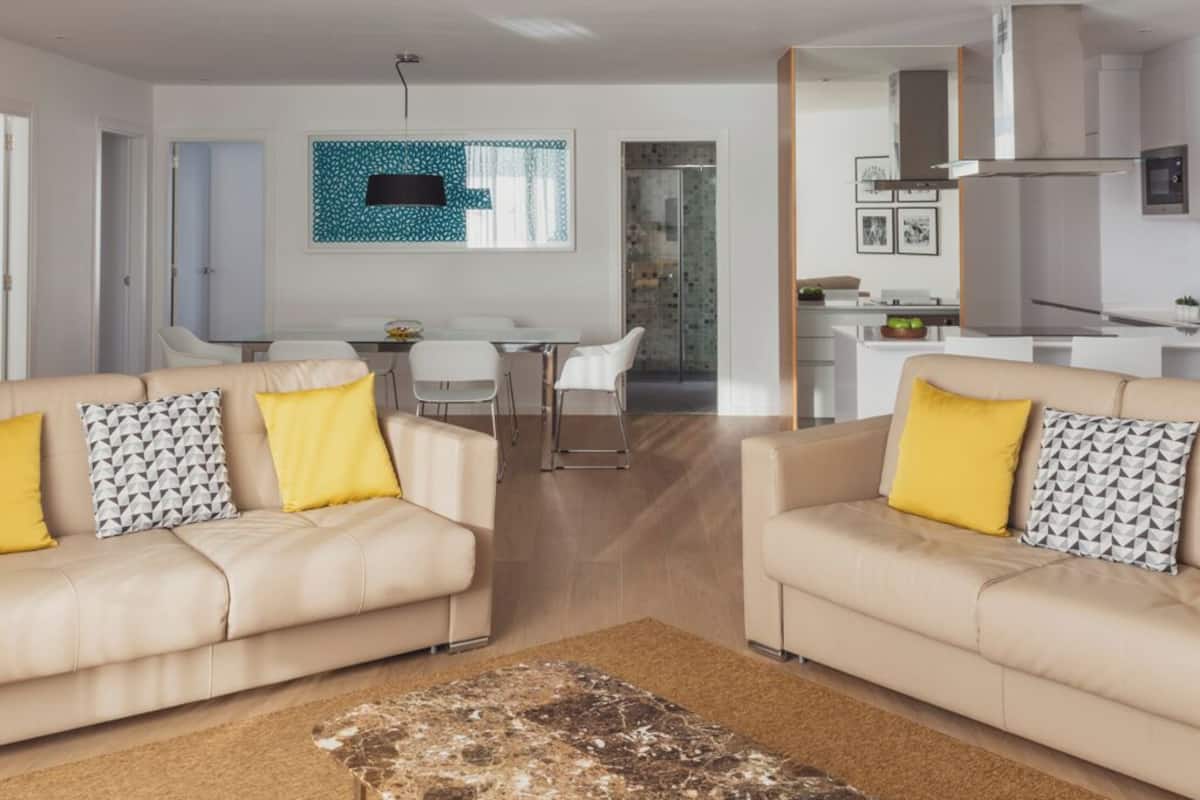 A modern living room with two beige sofas, a coffee table, and a dining area with a glass table and chairs.