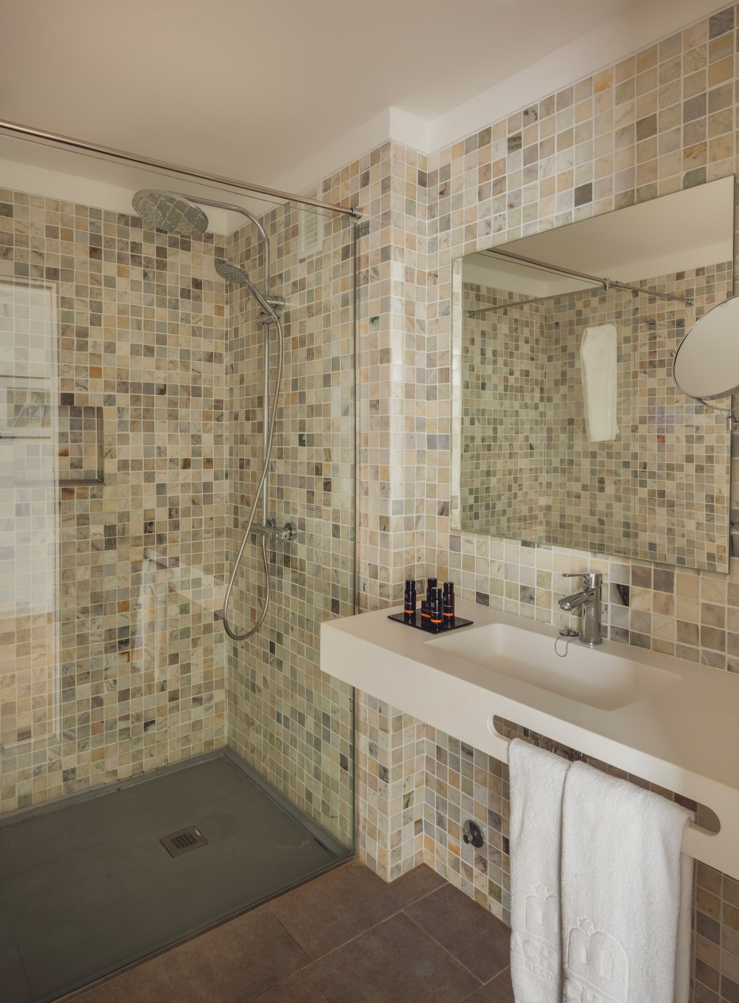 Ein Badezimmer mit Wandfliesen aus Mosaik, einer Dusche, einem Waschbecken mit Pflegeprodukten und einem Handtuchhalter.