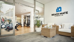Interior de un gimnasio con equipo de ejercicio, una zona de recepción y un área de descanso con una planta.