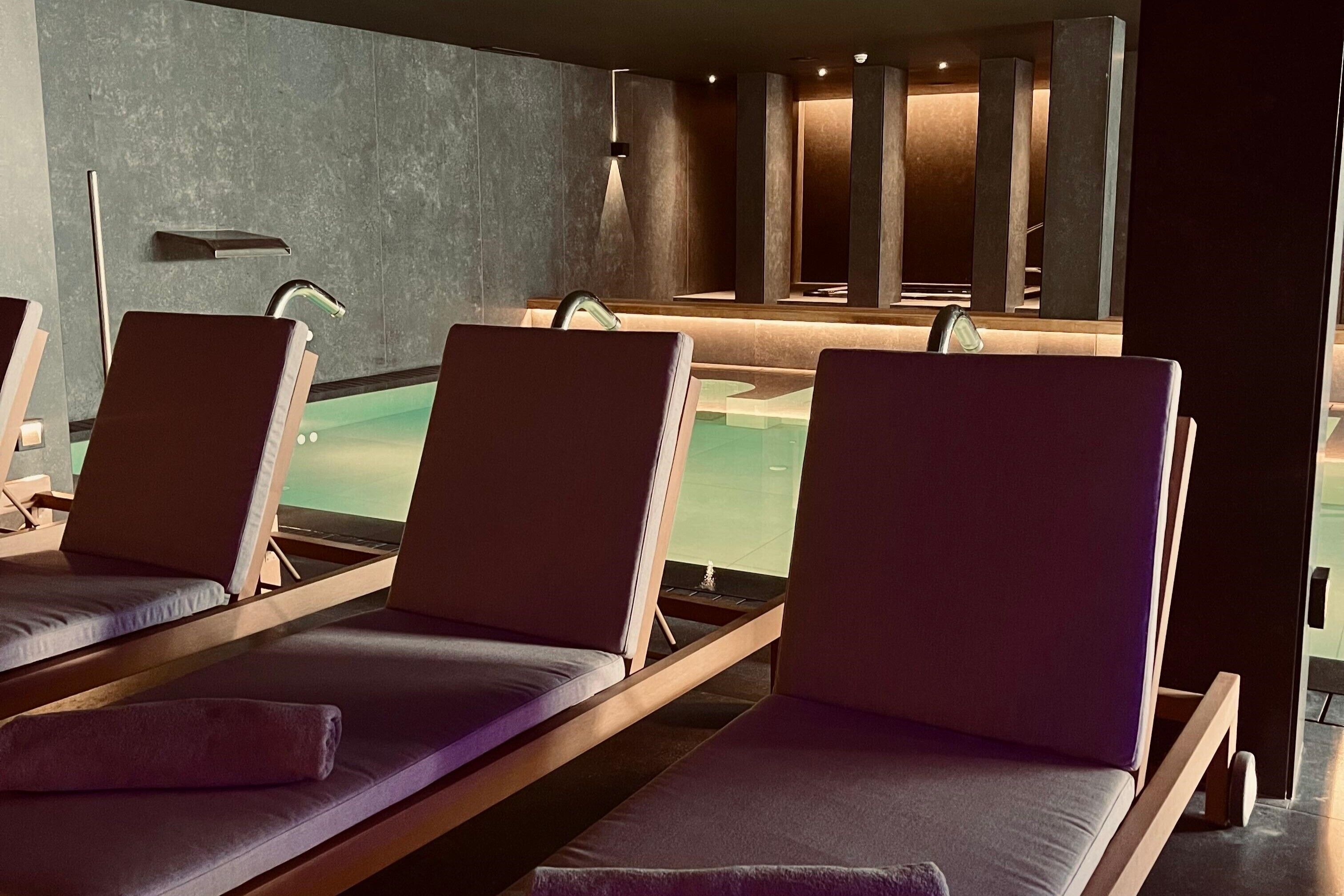 A spa area with three sun loungers, a small pool, and a mirror reflecting the space.