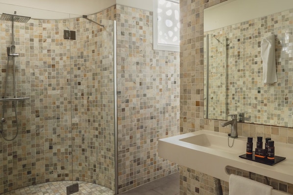 A bathroom with mosaic tile walls, a glass-enclosed shower, a sink with toiletries, and a mirror. - Flamingo Beach Mate (Adeje)