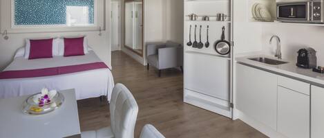A hotel room with a bed, a desk, a chair, a kitchenette with a microwave, and a bathroom.