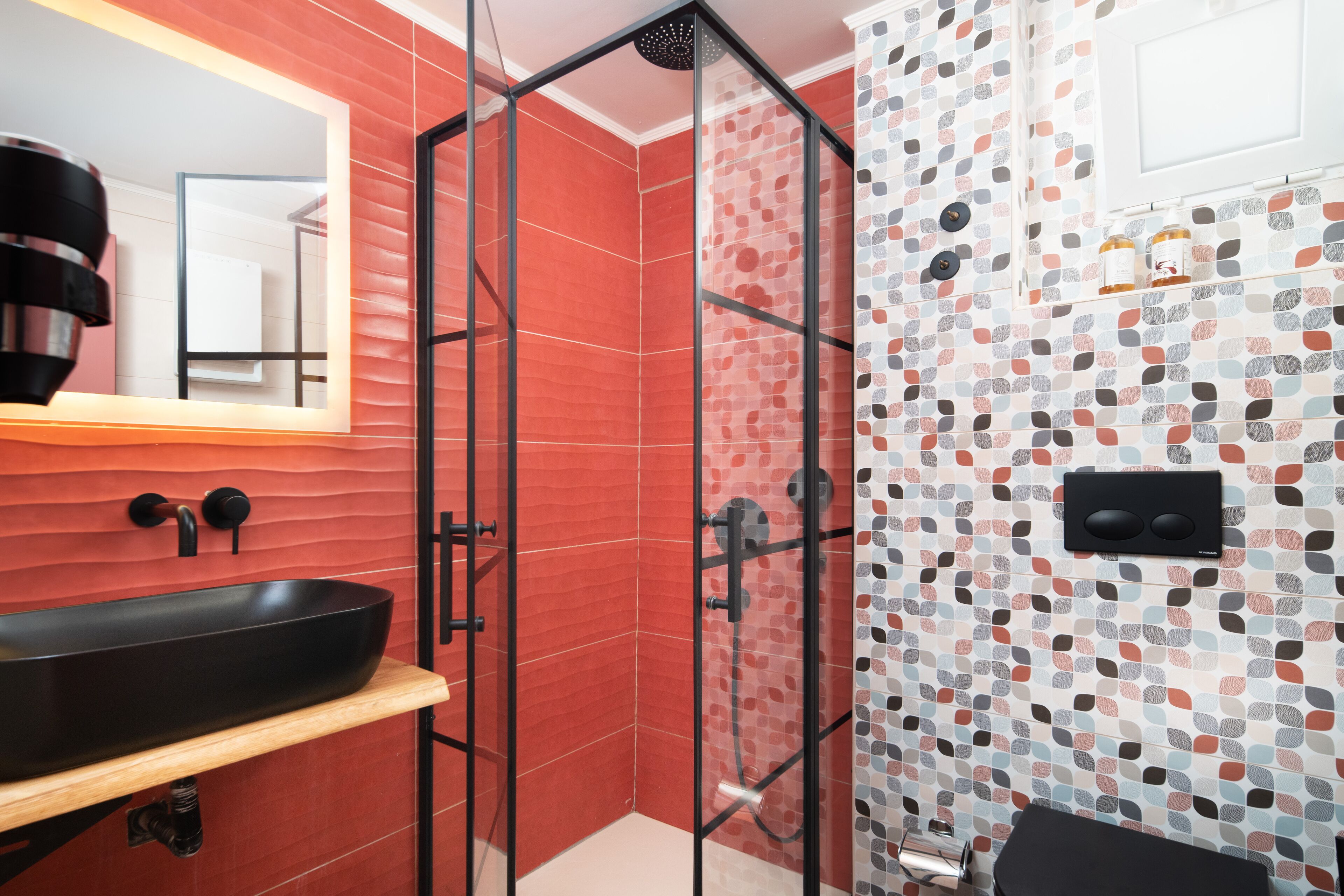 Une salle de bain moderne avec une douche à parois de verre, un lavabo noir et un mur recouvert de carreaux formant un motif géométrique.