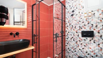A modern bathroom with a glass-enclosed shower, a black sink, and a tiled wall with a geometric pattern.