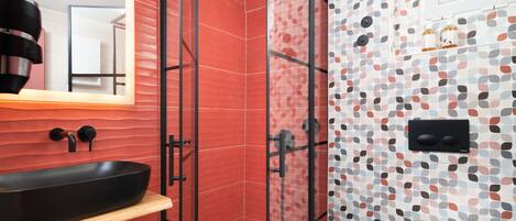 A modern bathroom with a glass-enclosed shower, a black sink, and a tiled wall with a geometric pattern.