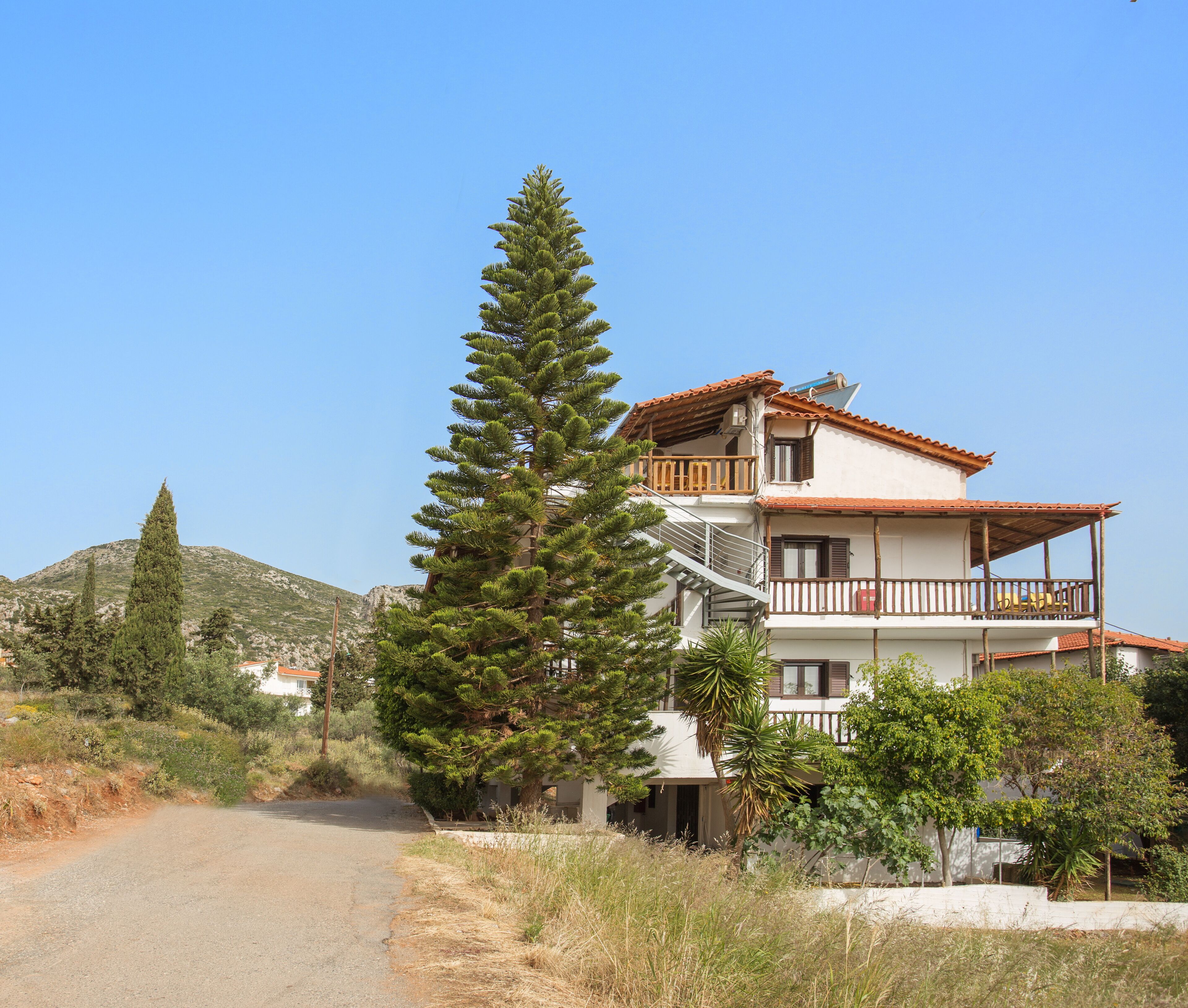 A two-story building with a balcony, surrounded by trees and a mountain in the background.