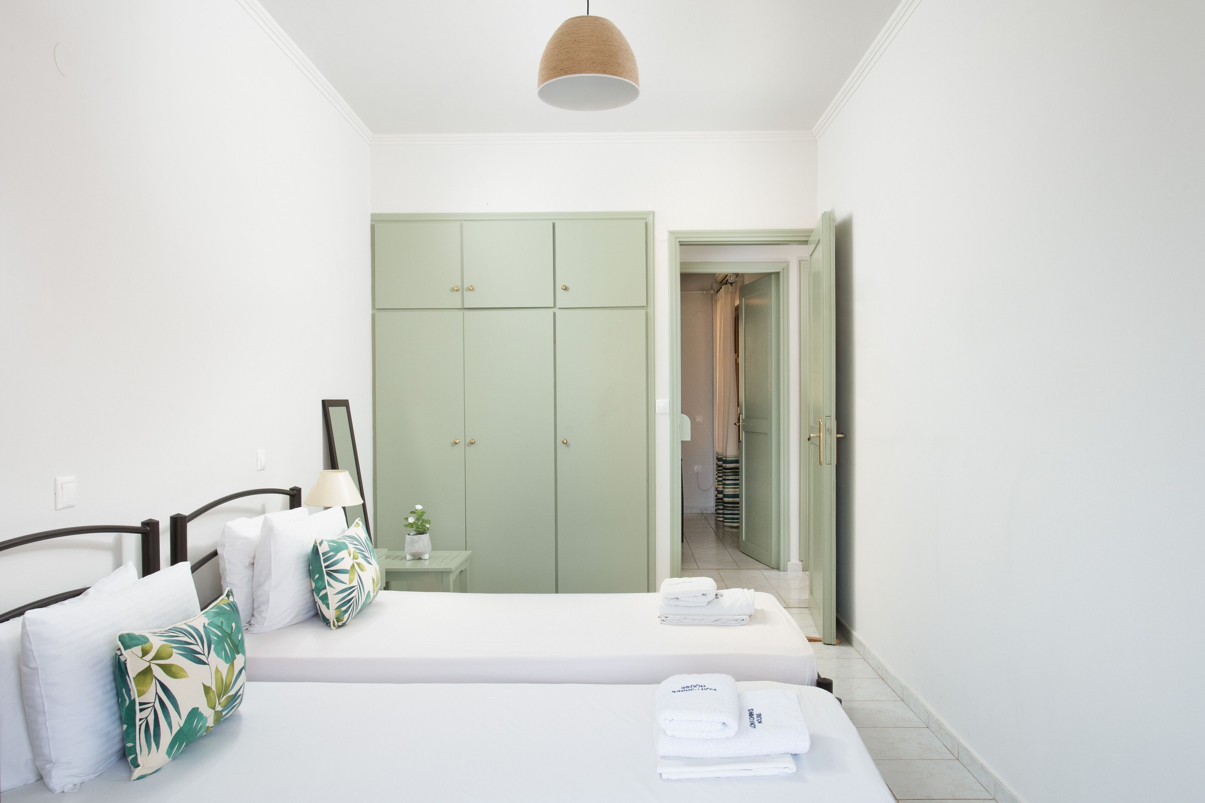 A bedroom with a bed, a nightstand, a green wardrobe, and a bathroom visible through an open door.