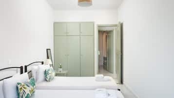 Un dormitorio con cama, mesita de noche, armario verde y baño a la vista a través de una puerta abierta.