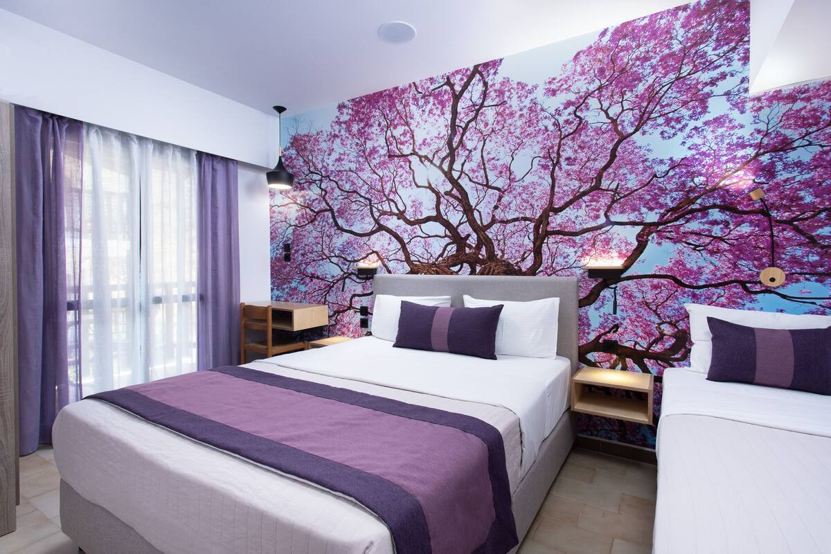 A bedroom with a large bed, two bedside tables, a nightstand, a window with curtains, and a wall mural of cherry blossoms.
