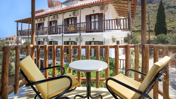 A balcony with wooden railings, a round table, and two yellow cushioned chairs. - Monemvasia Green Apartments (Monemvasia)