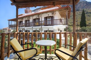 A balcony with wooden railings, a round table, and two yellow cushioned chairs. - Monemvasia Green Apartments (Monemvasia)