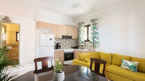 A modern kitchen with wooden cabinets, a white refrigerator, and a dining table with chairs. - Monemvasia Green Apartments (Monemvasia)
