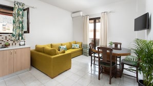 A compact living space with a sofa, dining table, chairs, a small kitchen area, and a TV mounted on the wall. - Monemvasia Green Apartments (Monemvasia)