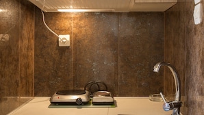 A compact kitchen with wooden cabinets, a built-in stove, a sink, and a compact refrigerator. - Monemvasia Green Apartments (Monemvasia)