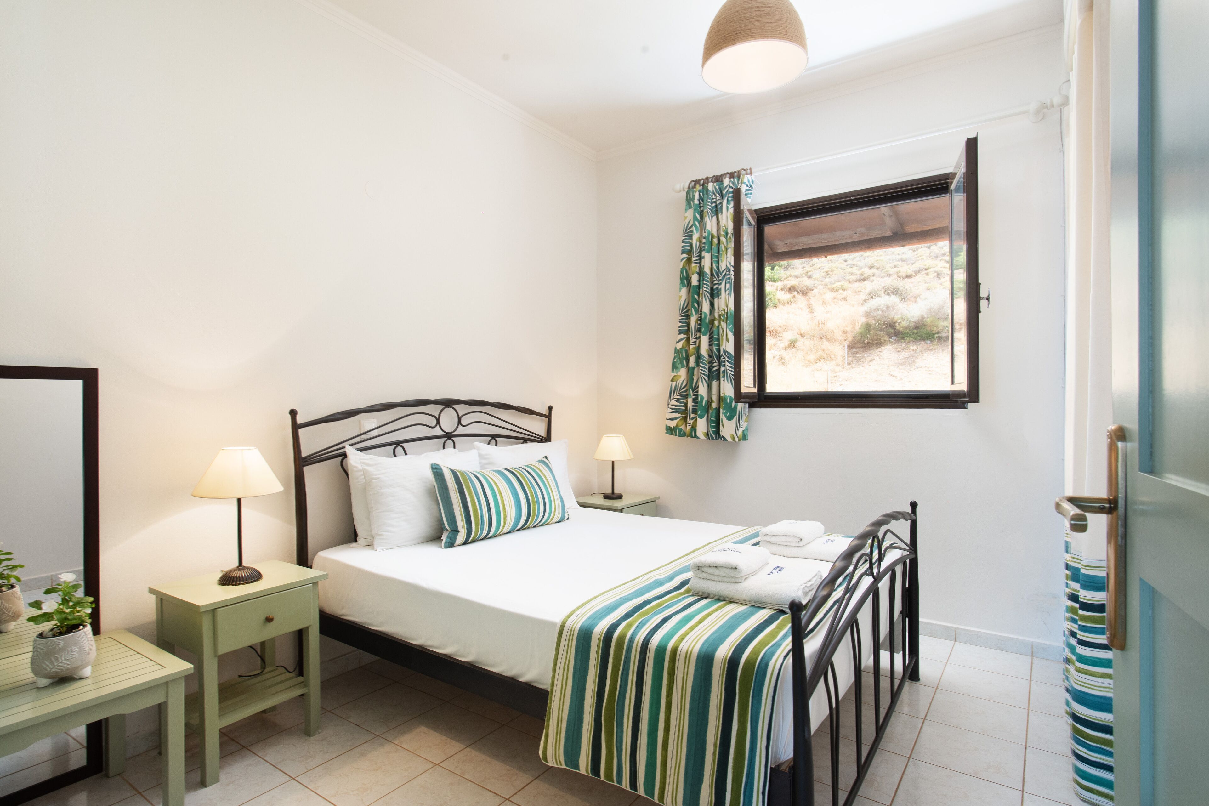Un dormitorio con cama, mesitas de noche, una ventana con cortinas y vistas al exterior.