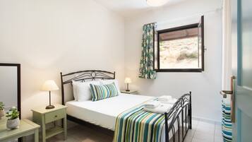 Un dormitorio con cama, mesitas de noche, una ventana con cortinas y vistas al exterior.