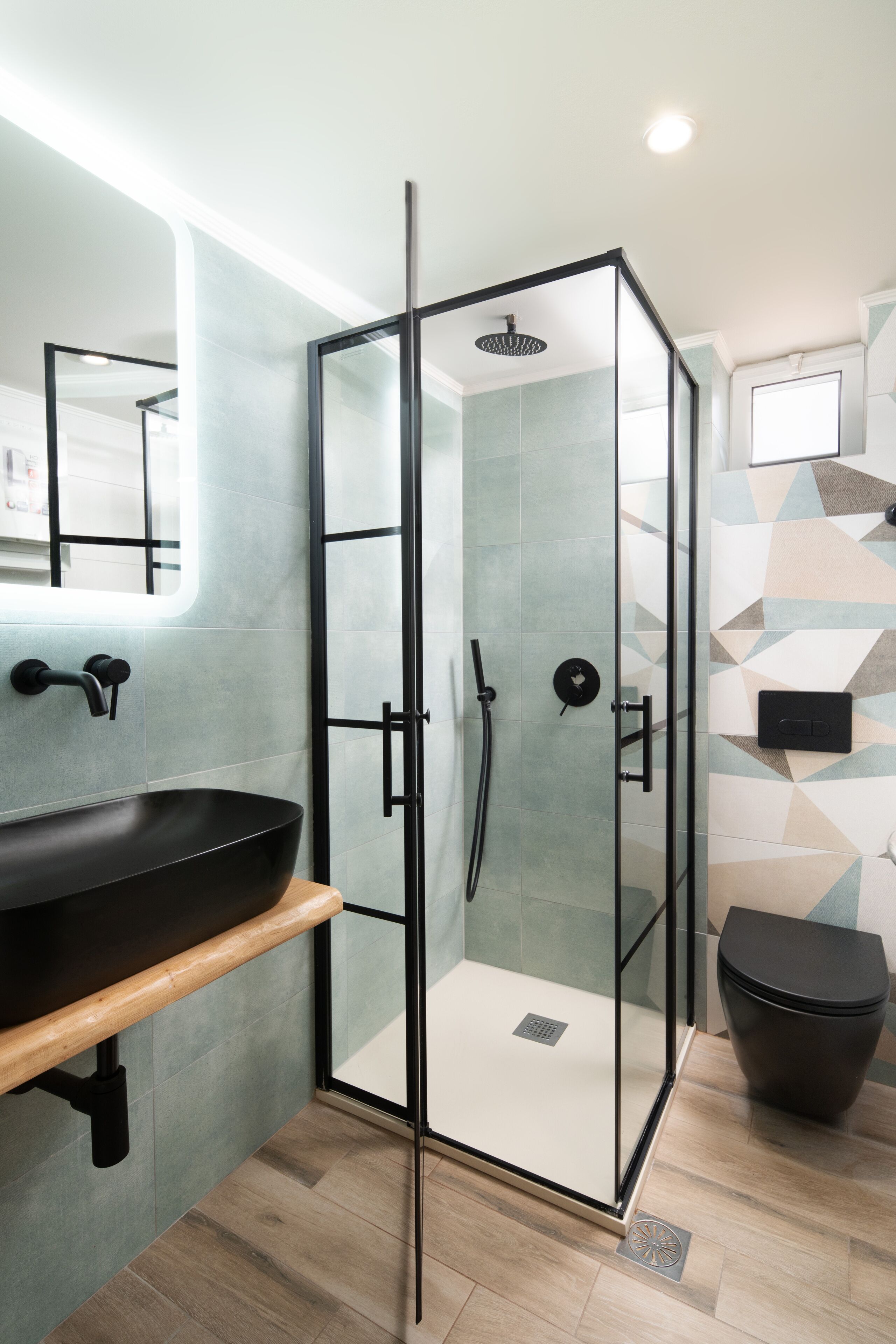 Un baño moderno con ducha envuelta en vidrio, lavabo negro y retrete.