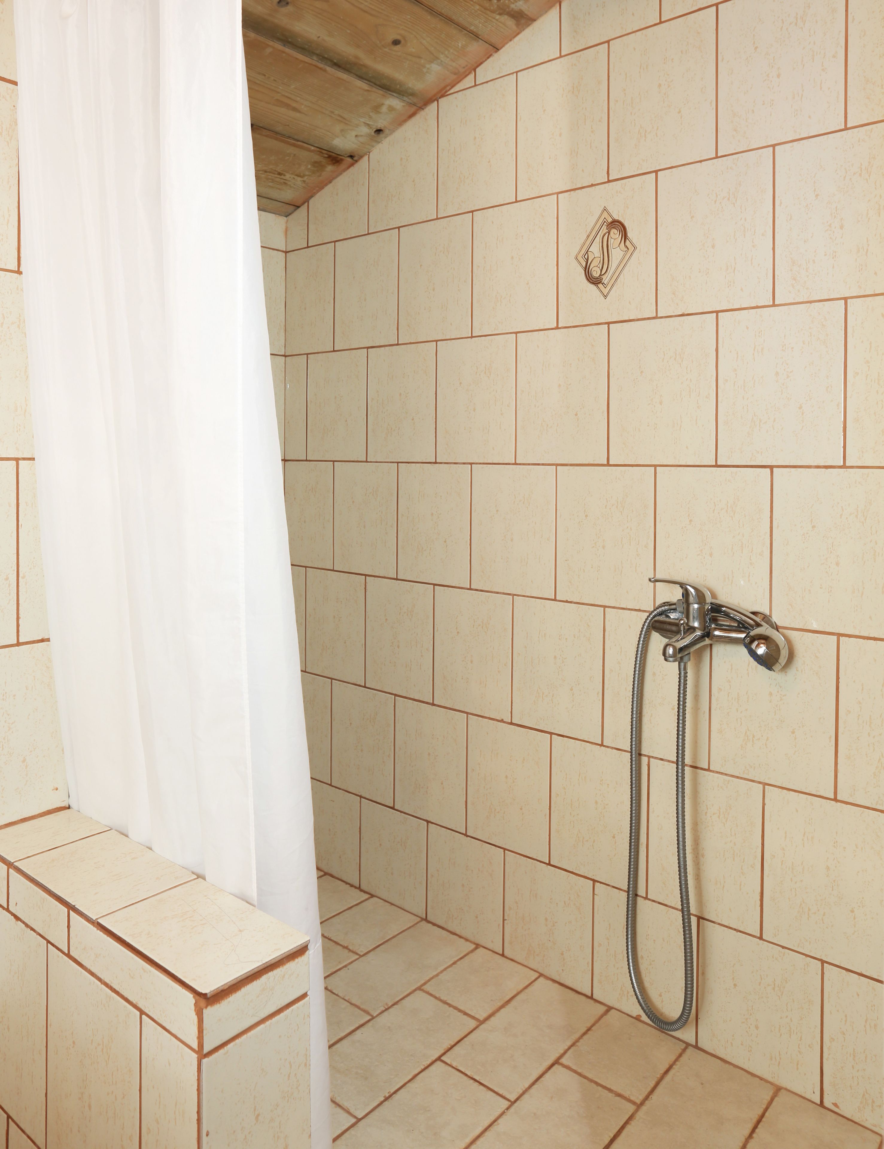 Un área de ducha con azulejos color beige, un cabezal de ducha y una cortina.