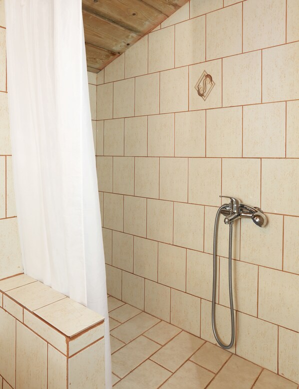 A shower area with beige tiles, a showerhead, and a curtain. - Monemvasia Green Apartments (Monemvasia)