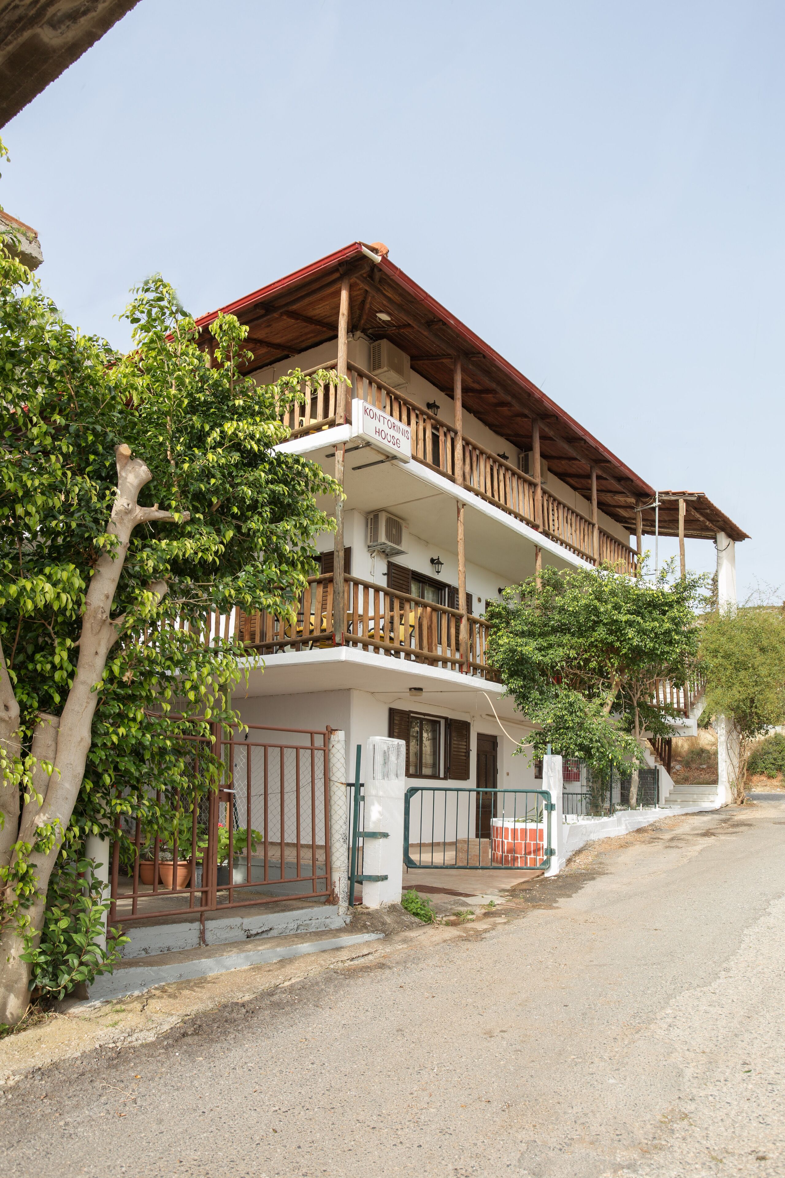 A two-story building with a wooden balcony, a gated entrance, and potted plants.