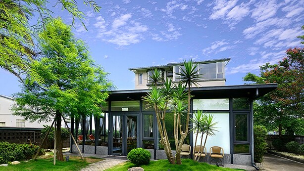 A modern house with a glass facade, a paved driveway, and a well-maintained garden. - Pokara Resort (Jiaoxi)