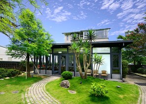 Una casa moderna con fachada de vidrio, camino de entrada pavimentado y un jardín cuidado.