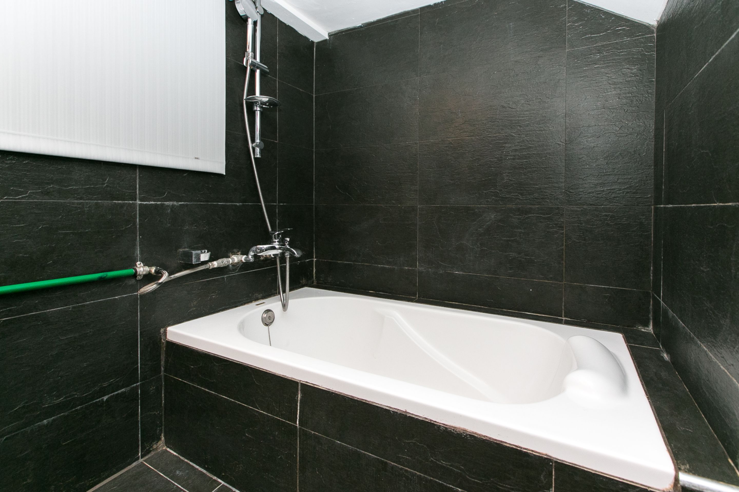 A modern bathroom with a freestanding bathtub, dark tiled walls, and a green towel rack.