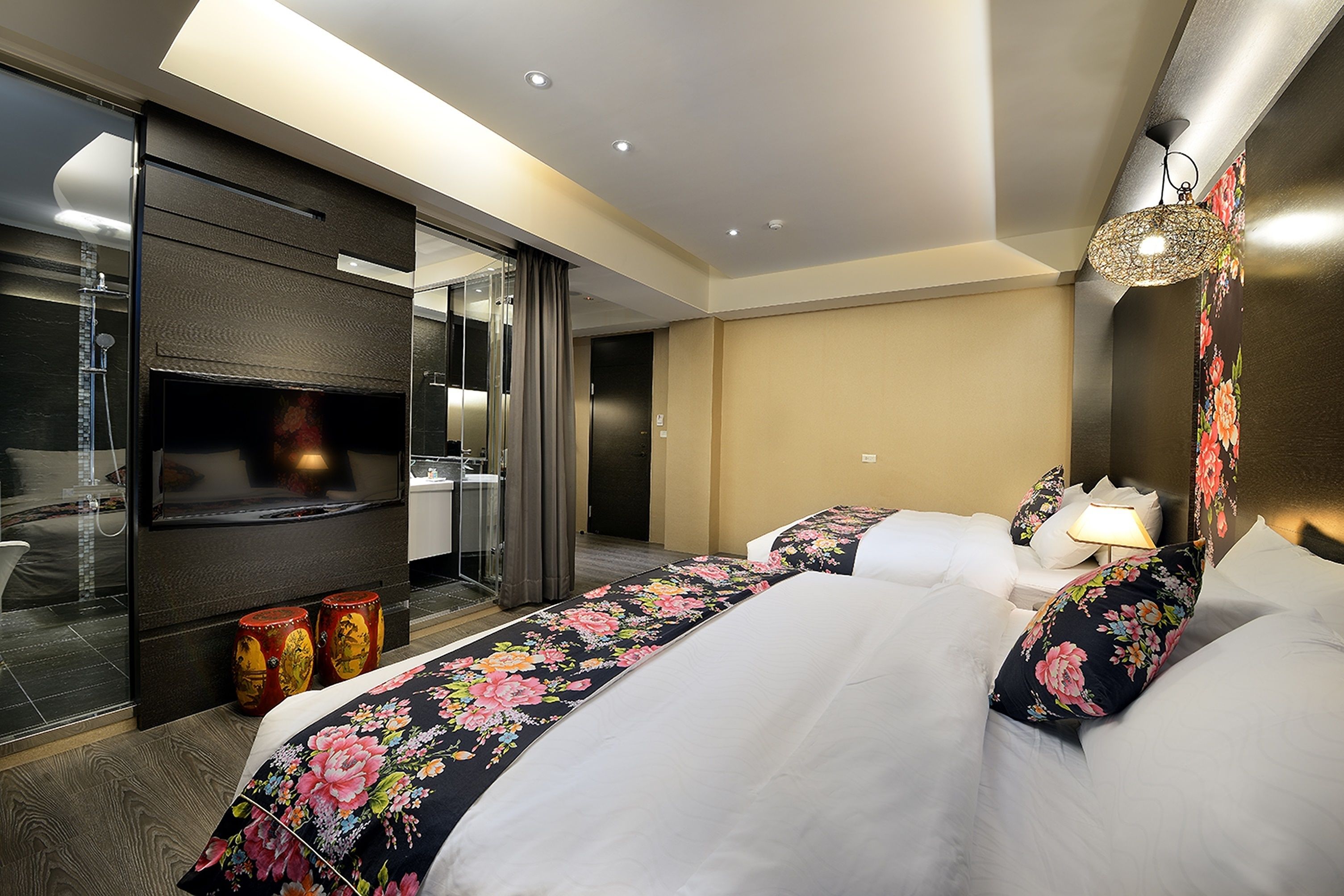Habitación de hotel con una cama grande, televisión, espejo y baño visible a través de un separador de vidrio.