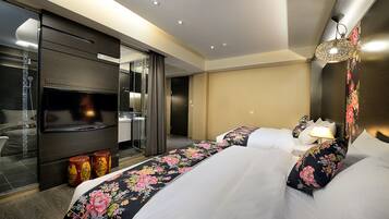Habitación de hotel con una cama grande, televisión, espejo y baño visible a través de un separador de vidrio.