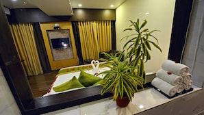 Habitación de hotel con un espejo grande, una planta en maceta, una cama con almohadas verdes y una pila de toallas.