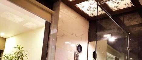 A modern bathroom with a glass shower enclosure, a marble-tiled wall, and a potted plant.