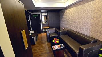 A modern hotel lobby with a dark wood floor, leather seating, a magazine on a coffee table, and patterned wallpaper.