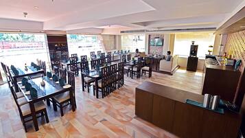 Un grand espace dédié à la restauration, avec plusieurs tables et chaises, un comptoir d’accueil et un coin cuisine.