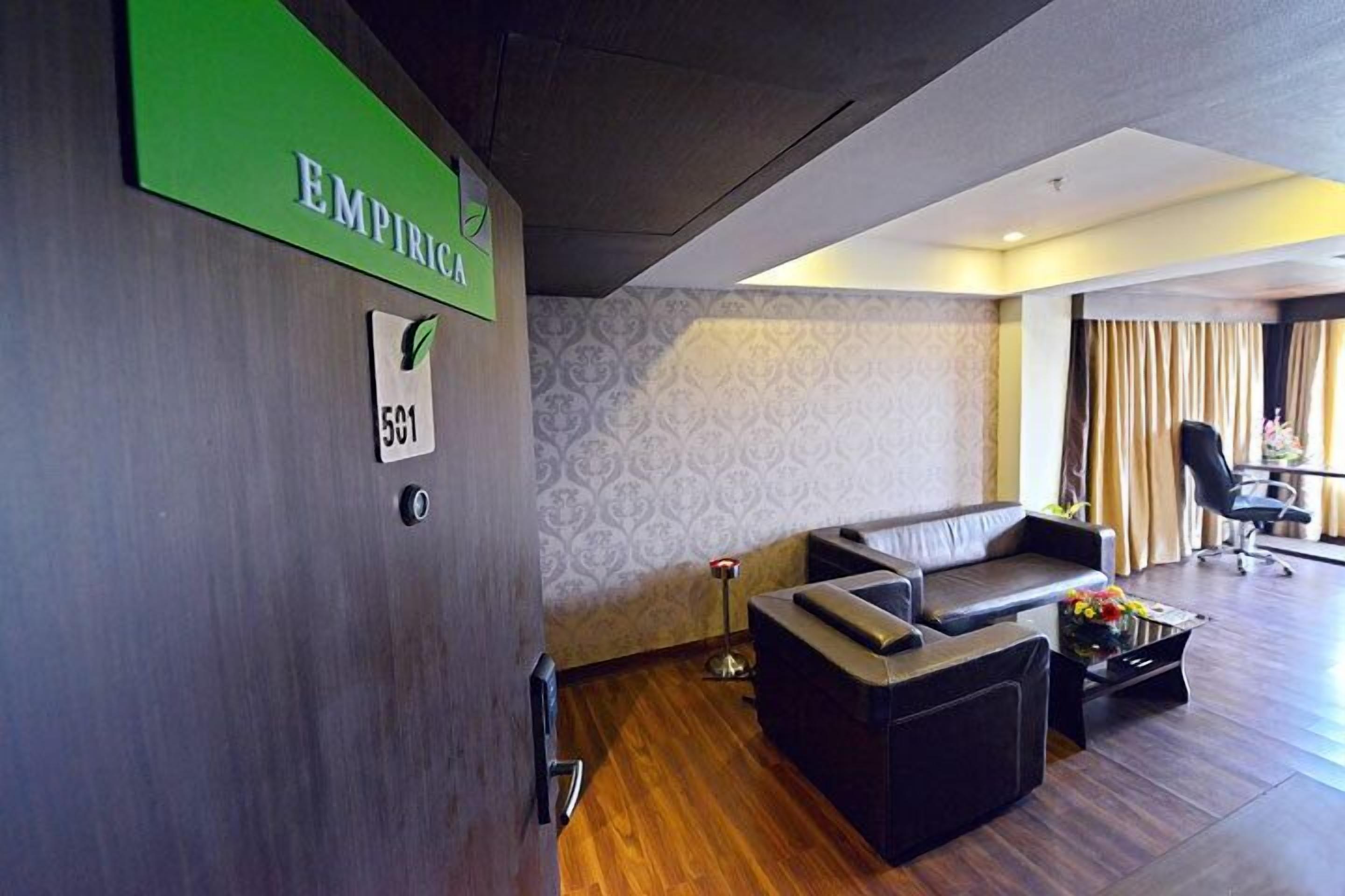 Un vestíbulo de hotel con una recepción, un sofá, una mesita de café y una pared decorada con un papel tapiz estampado.